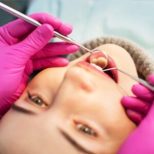 Persona recibiendo un examen dental, con el dentista sosteniendo herramientas en ambas manos, usando guantes rosas.