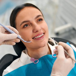 Mujer sonriente recibiendo un chequeo dental, mientras el dentista examina su boca usando un espejo dental y otro instrumento.